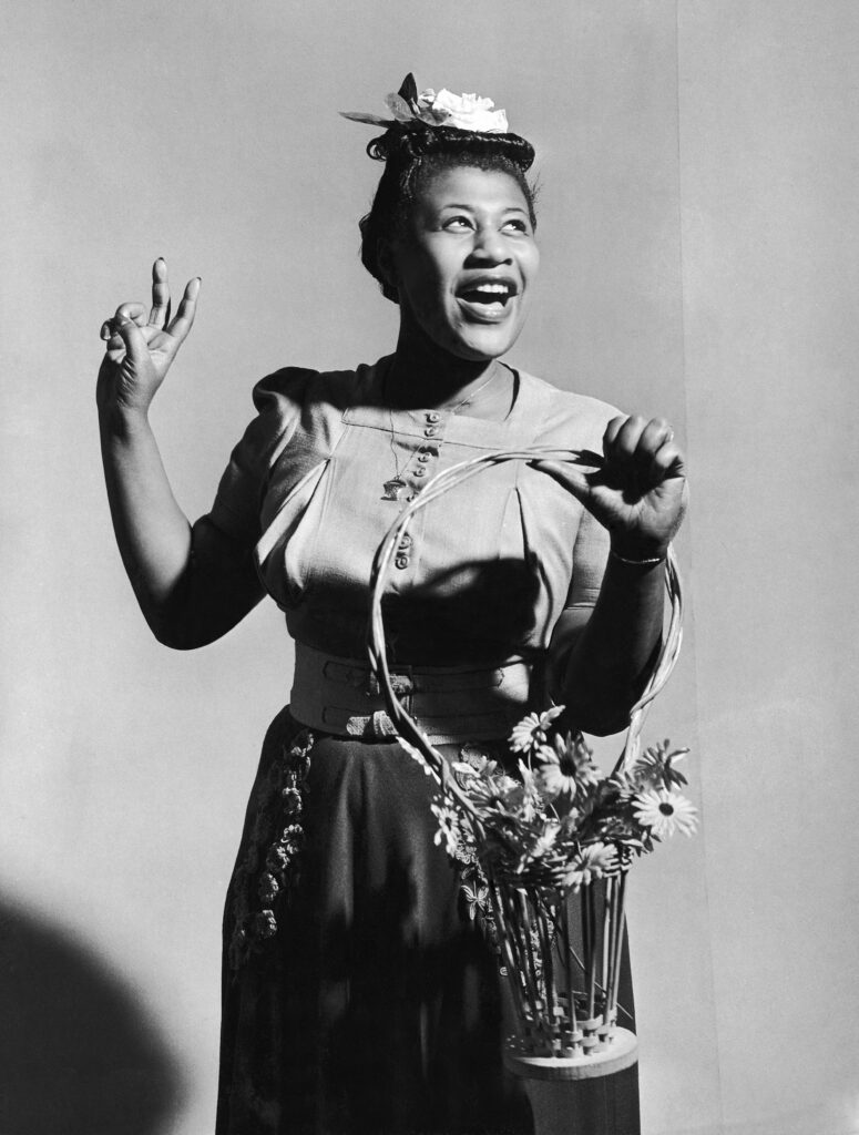Singer Ella Fitzgerald holding a basket of flowers as she sings A-Tisket, A-Tasket in front of backdrop, 1946.